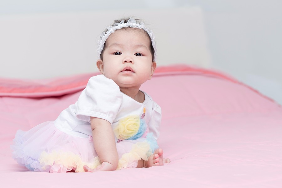 06. Aziatische baby van 6 maanden oud zit en leunt op haar armpje